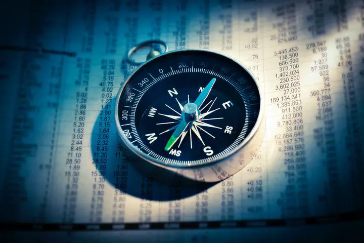 Photo shows a compass over a sheet of numbers, illustrating use of AI to guide decisions